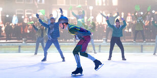 Een schaatser  schaatst voorovergebogen op een ijsbaan. Aan de kant en op het ijs staan mensen met de armen in de lucht