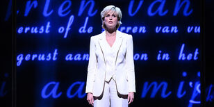 Diana in wit mantelpak, achter haar een scherm met blauwe letters