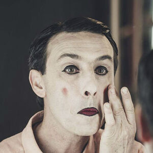 Een clown brengt witte make up aan op zijn gezicht. 