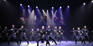 12 in sjiek zwart geklede dansers met op de achtergrond de band Blaudzun op een verhoging