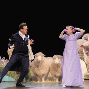Voor een kudde schapen danst een man in een zwart pak en een man in een lange roze jurk.