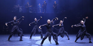 Zeven dames in het zwart dansen, achter hen een live band