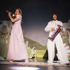 Een man en een vrouw zingen uit volle borst, staande tussen de schapen.