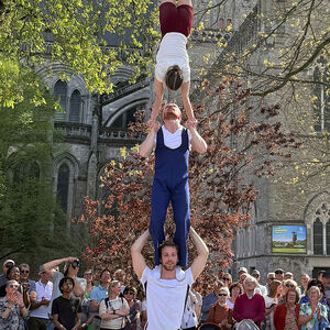 Drie acrobaten staan op elkaar. De bovenste acrobate staat op haar kop. 