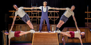 gekleed in turnkleding staan vijf acrobaten in molenwiek pose op een houten gymnastiekkast