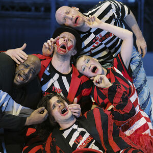 De groep acteurs en dansers in gestreepte kleren houden elkaar vast terwijl ze huilen. 