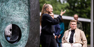 Een stenen kunstwerk met een groot rond gat en ernaast een vrolijke danseres.
