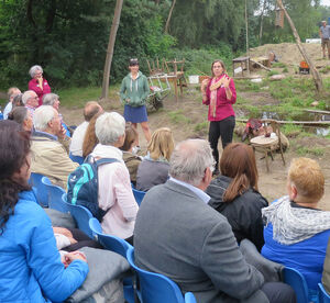 introductie bij de openluchtvoorstelling Chasse Patate van Studio Orka: Angelique staat voor de groep, met het decor op de achtergrond