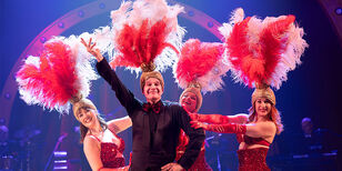 Ons pap wil bij de revue Arie Cupé met een prachtige veren showtooi op zijn hoofd neemt samen met drie jongere showgirls stralend een showpose aan