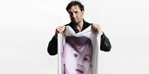 Acteur Jeroen Spitzenberger houdt een laken omhoog met daarop een zwartwit foto van een kindergezicht.