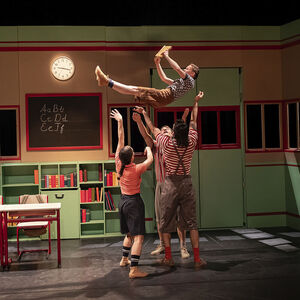 Al boeklezend wordt een acrobaat hoog in de lucht geworpen door drie anderen.