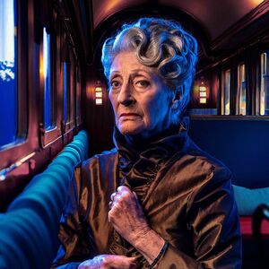 Oudere dame met keurig gekapt grijs haar, in een oude treinwagon.