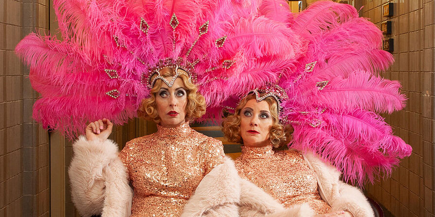 Plien en Bianca zitten in glitterjurken en grote hoofdtooien, alsof ze optreden in Las Vegas. Ze kijken verveeld. 
