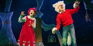 Foeksia in een rood jurkje en een rode puntmuts en Dolfje met woest wit haar met twee harige wolven-oortjes staan zingend naast elkaar.