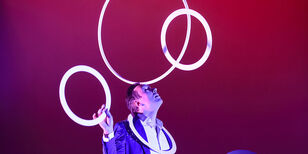 David jongleert witte ringen door een hoepel die op zijn voorhoofd balanceert